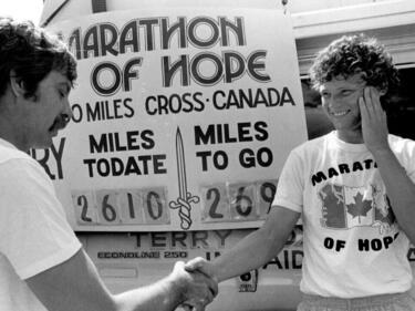 Terry Fox shaking hands in front of Marathon of Hope poster